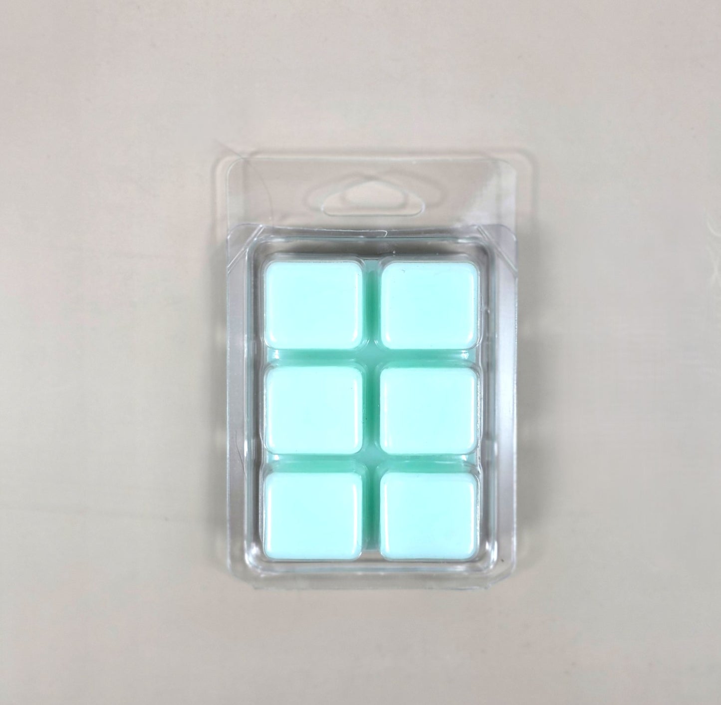 Underside view of a clear plastic 6-cube clamshell packaging showing light mint green soy wax melt cubes by Smell Good Candles.