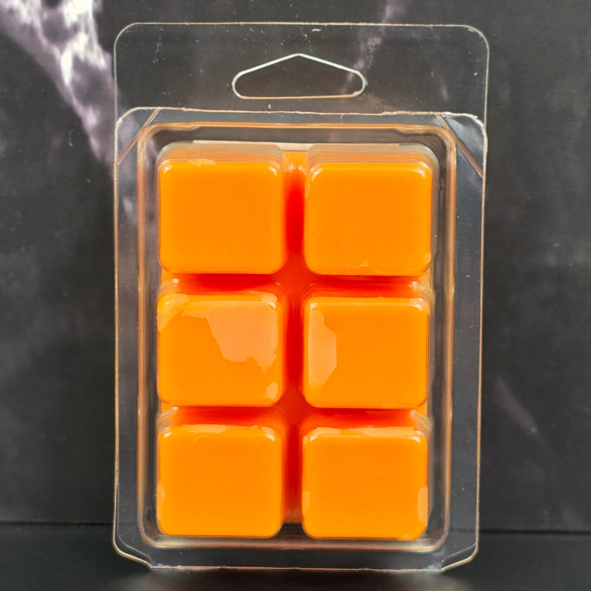 Pack of six orange wax melts in clear packaging on a dark marble surface