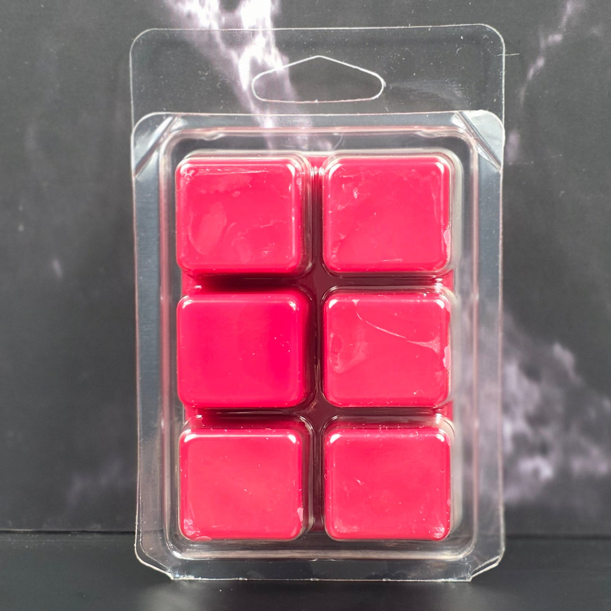 Pack of six red wax melts in clear packaging on a dark marble surface
