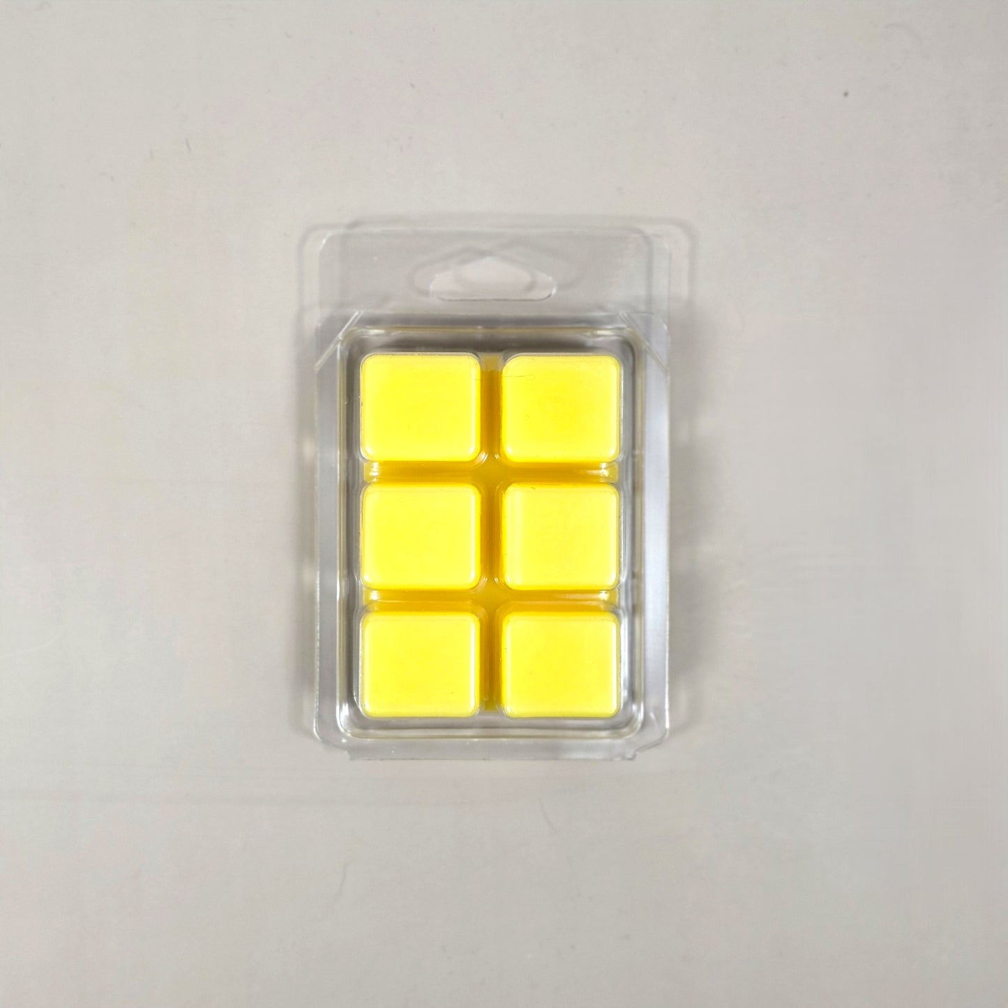 Underside view of a clear plastic 6-cube clamshell package showing bright yellow soy wax melt cubes.