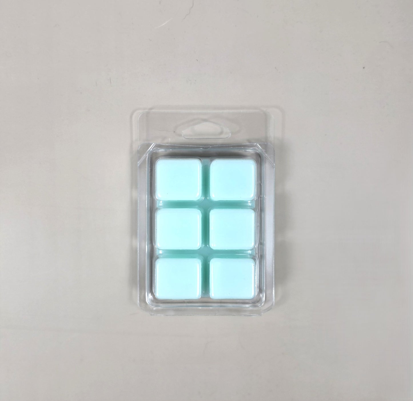 Underside view of a clear plastic 6-cube clamshell packaging showing light aqua blue soy wax melt cubes.