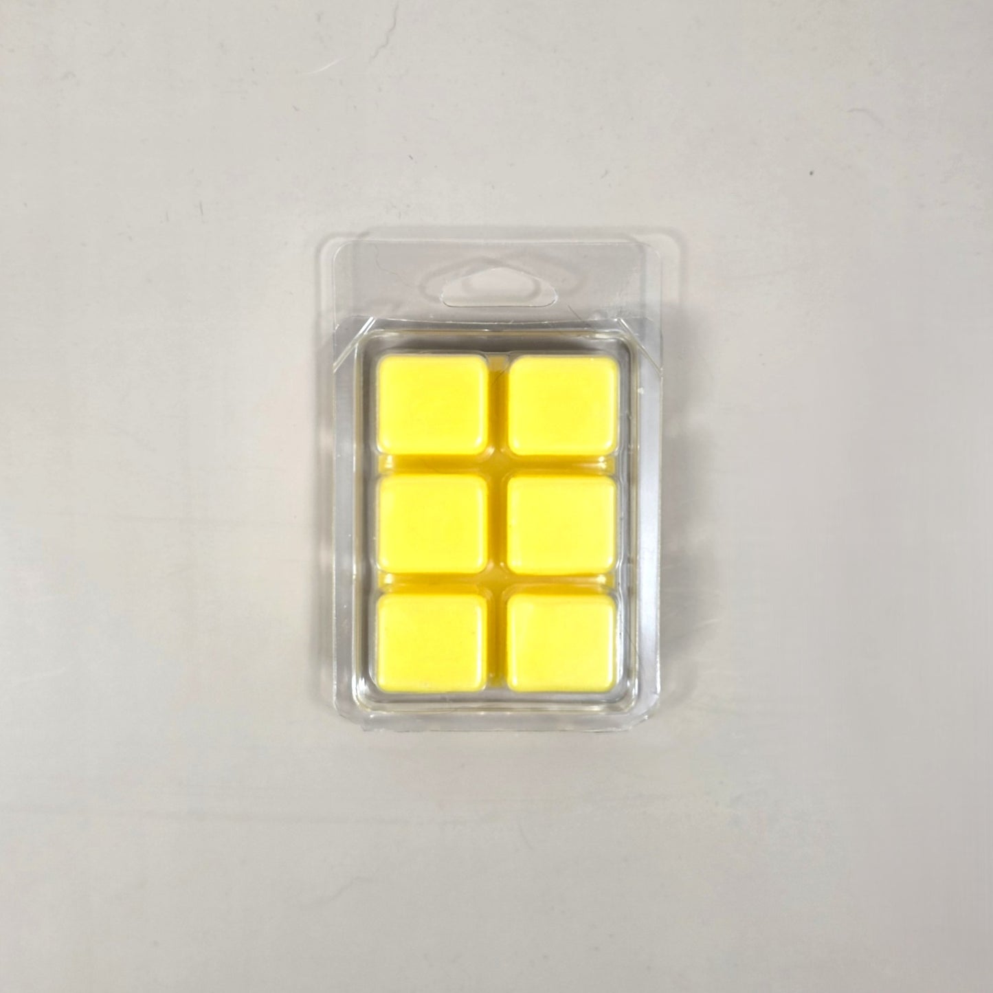 Underside view of a clear plastic 6-cube clamshell package filled with bright yellow soy wax melt cubes by Smell Good Candles.