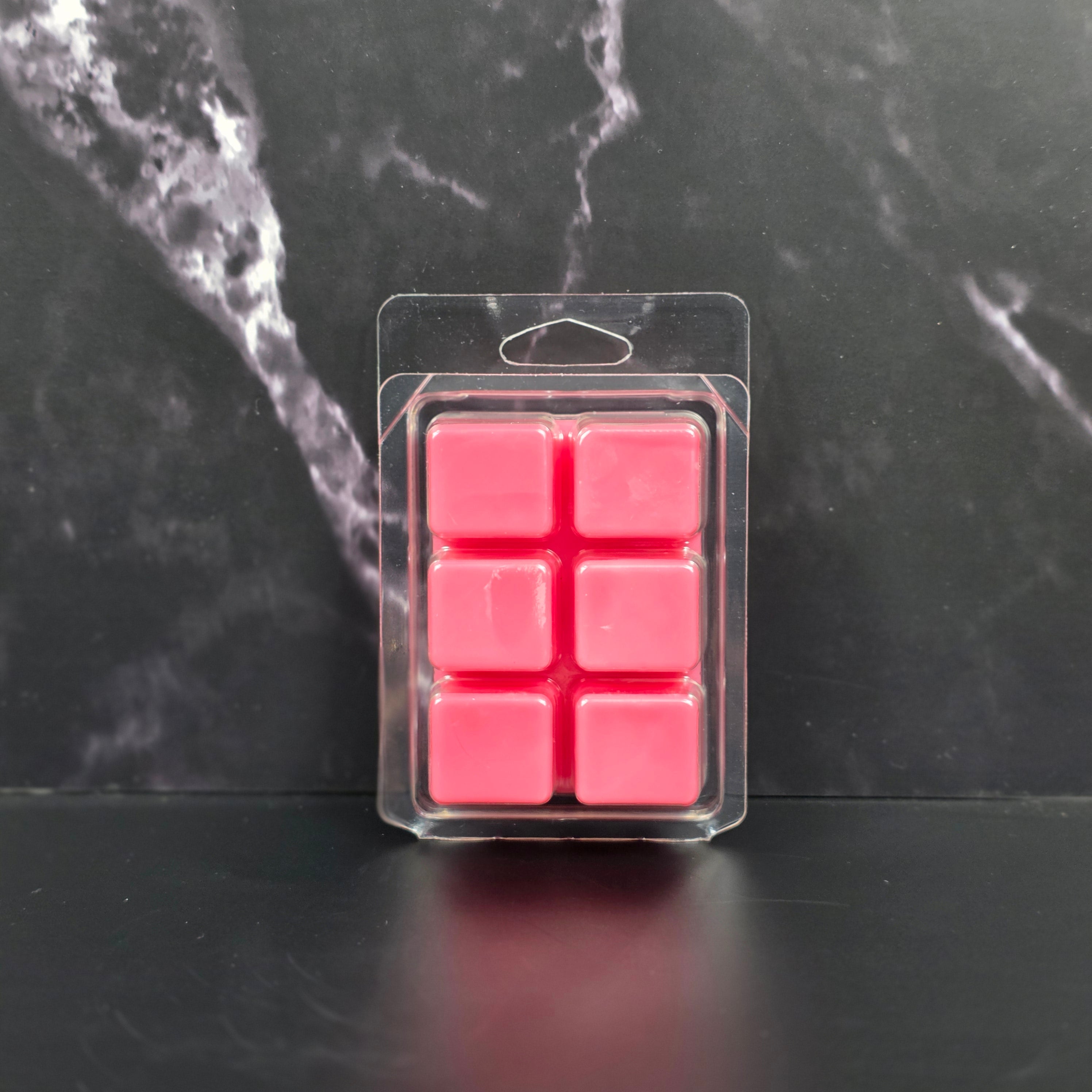 Pack of six pink wax melts in clear packaging on a black marble surface