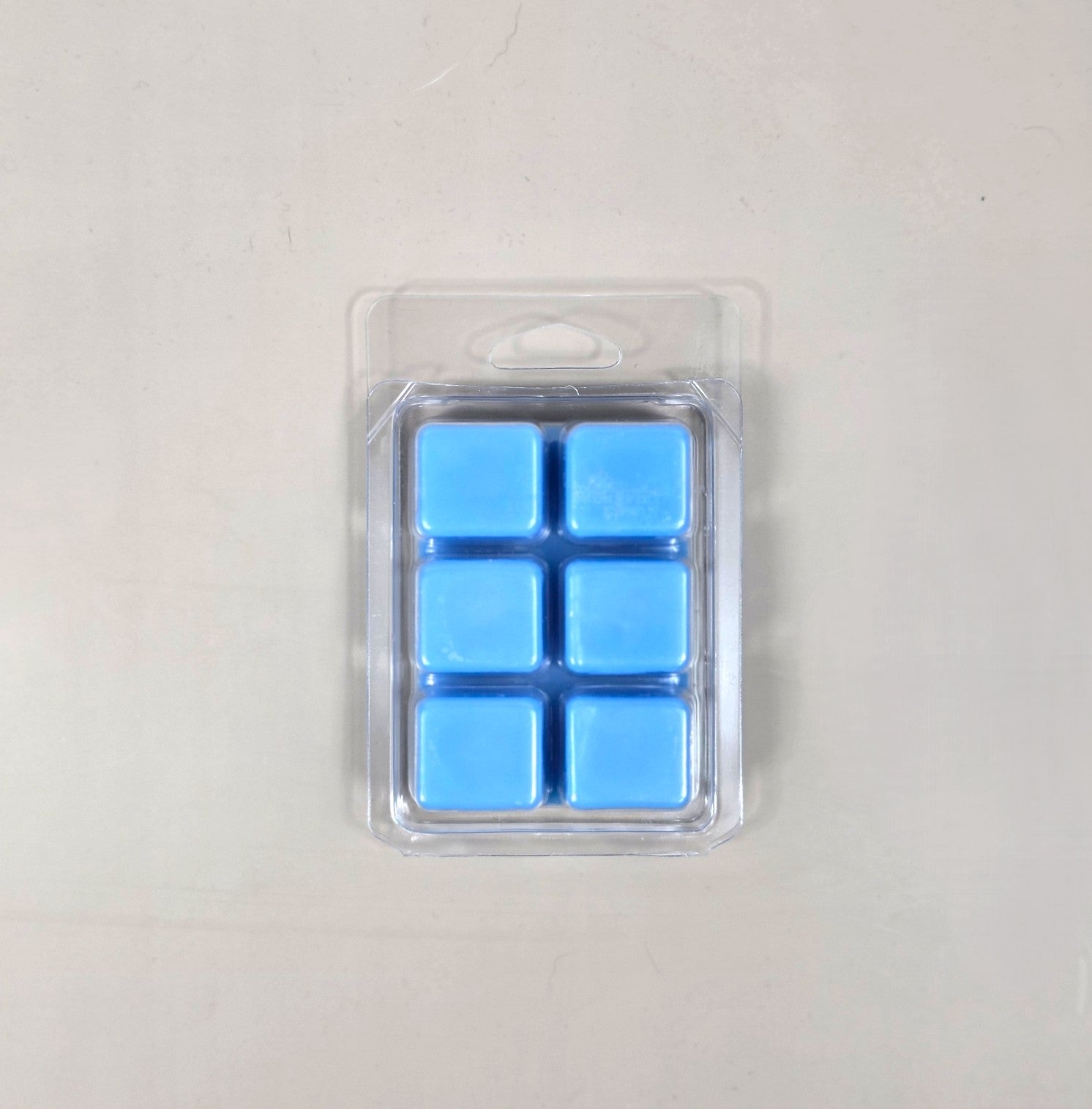 Underside view of a clear plastic 6-cube clamshell package showcasing soft sky blue soy wax melt cubes.