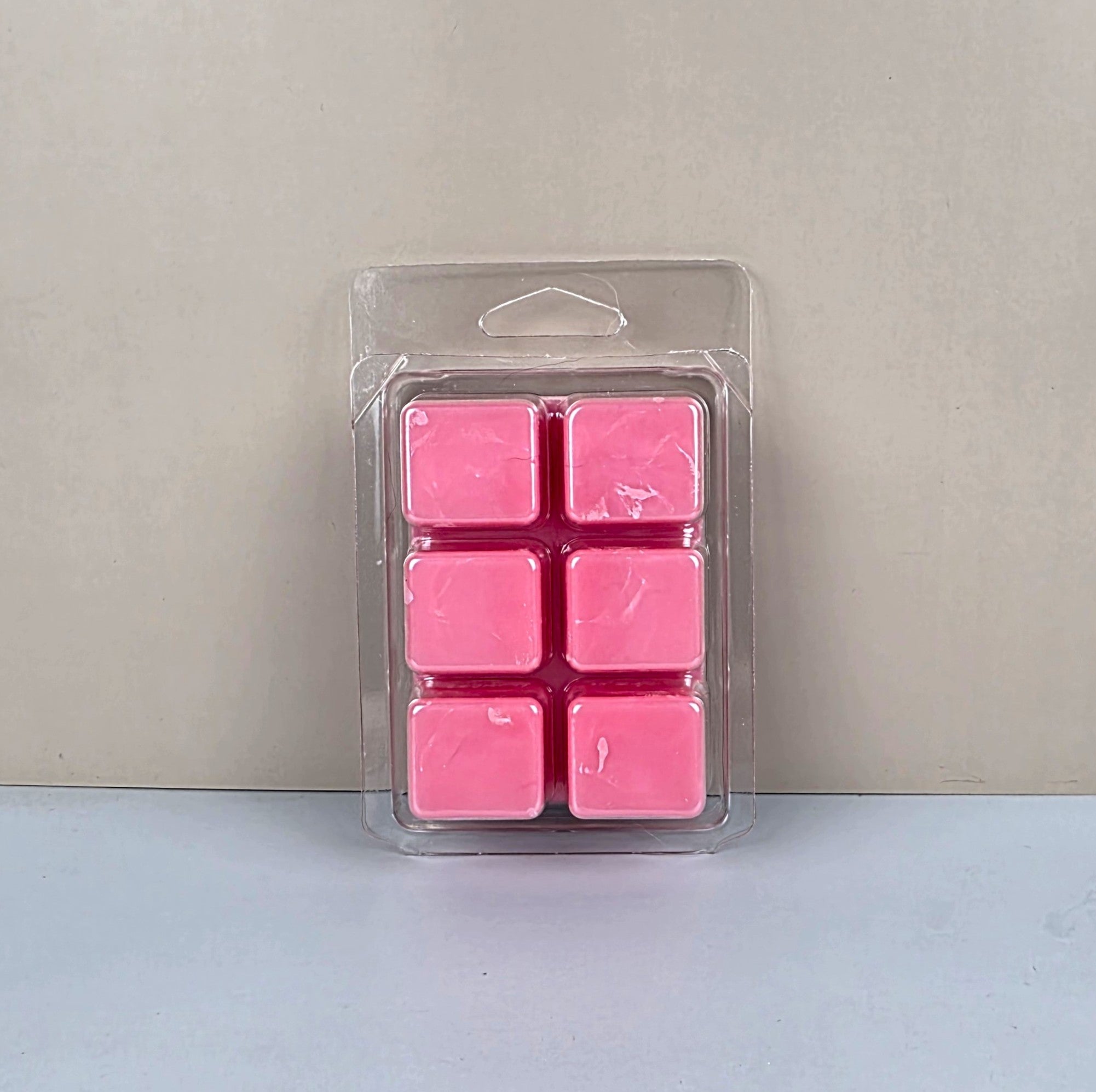 Pack of pink wax melts in clear packaging on a light gray background