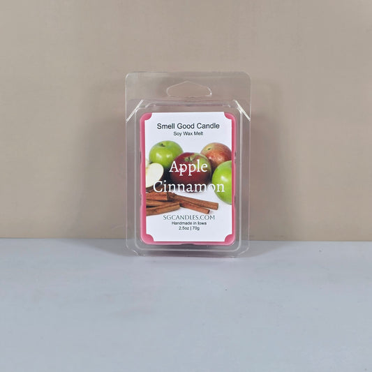 Labeled "Apple Cinnamon" Smell Good Candle 2.5oz soy wax melt in clamshell packaging. The label features vibrant graphics of apples and cinnamon sticks, highlighting the fragrance inspiration and handmade origin.