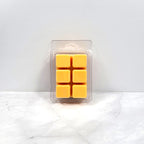 Pack of six yellow wax melts in a clear plastic packaging on a white marble surface.