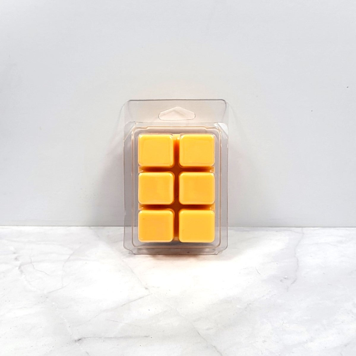 Pack of six yellow wax melts in a clear plastic packaging on a white marble surface.