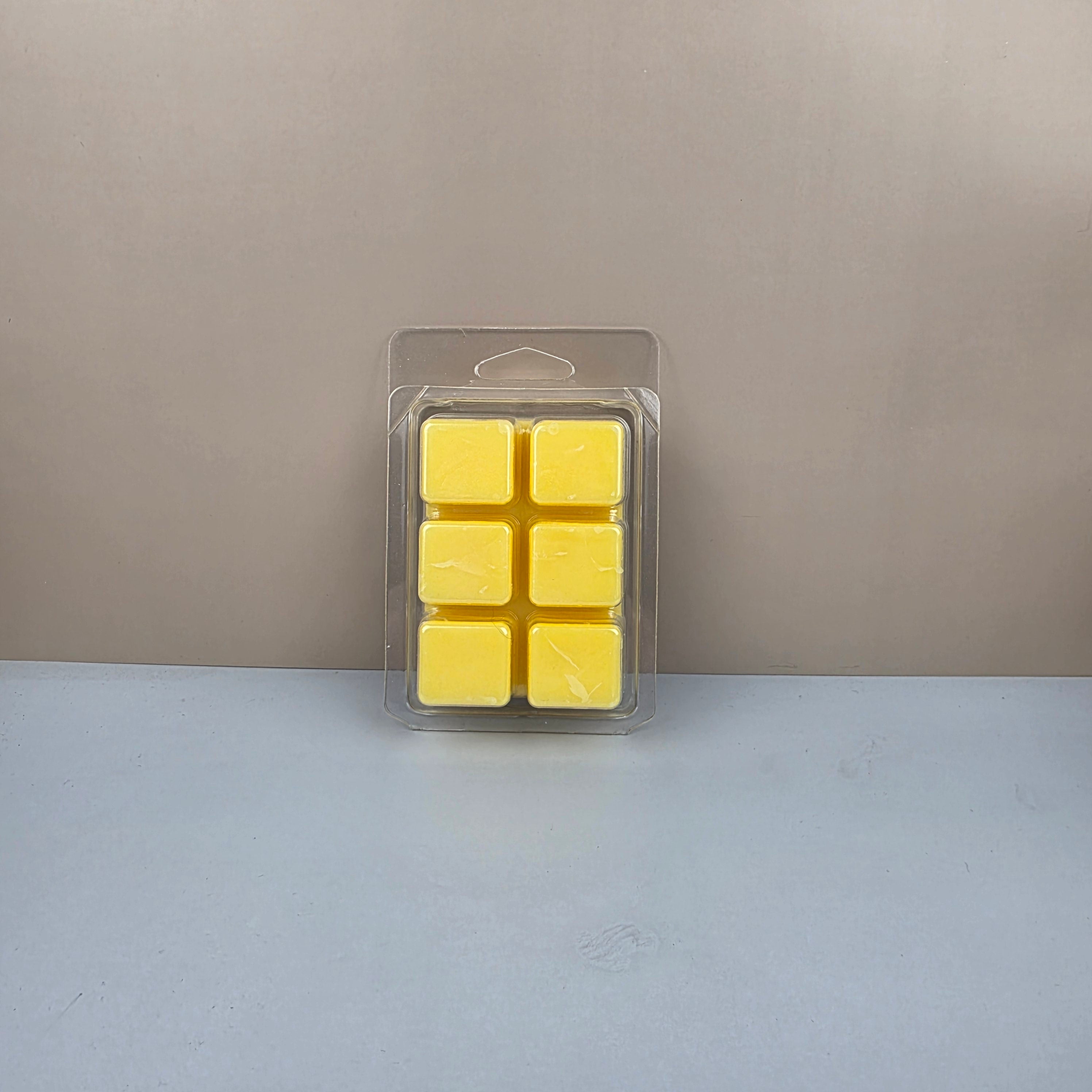 Pack of six yellow wax melts in clear packaging on a gray surface with a beige background