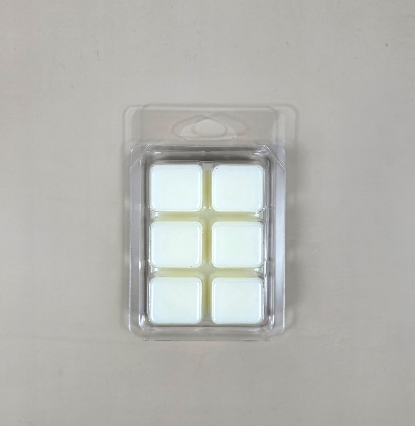 Underside view of a clear plastic 6-cube clamshell package showcasing creamy white soy wax melt cubes.