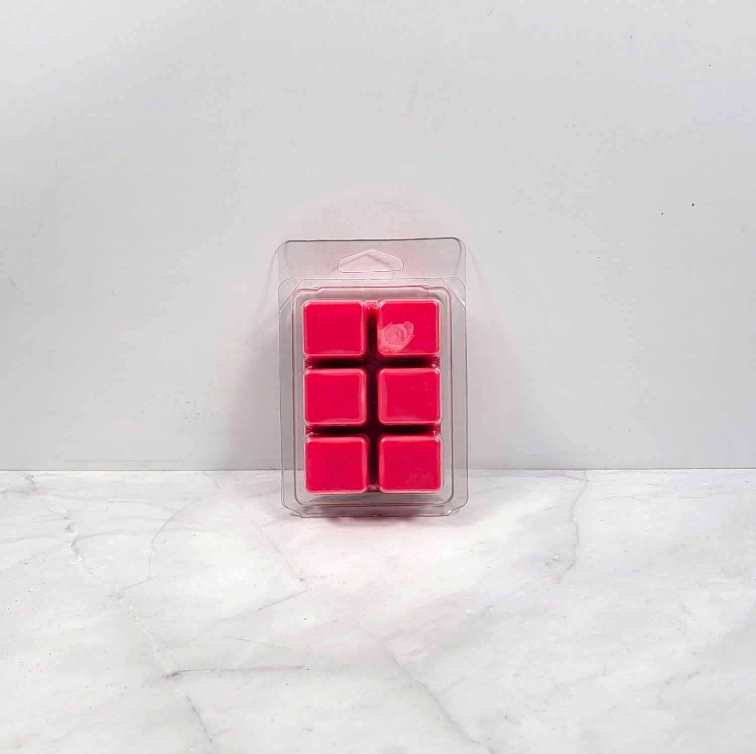 Pack of six pink wax melts in clear packaging on a white surface with a light gray background
