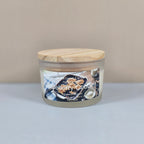 A 4oz clear glass jar candle with a black metal lid, featuring a "Blueberry Cobbler" label with a rustic illustration of a fresh blueberry dessert.
