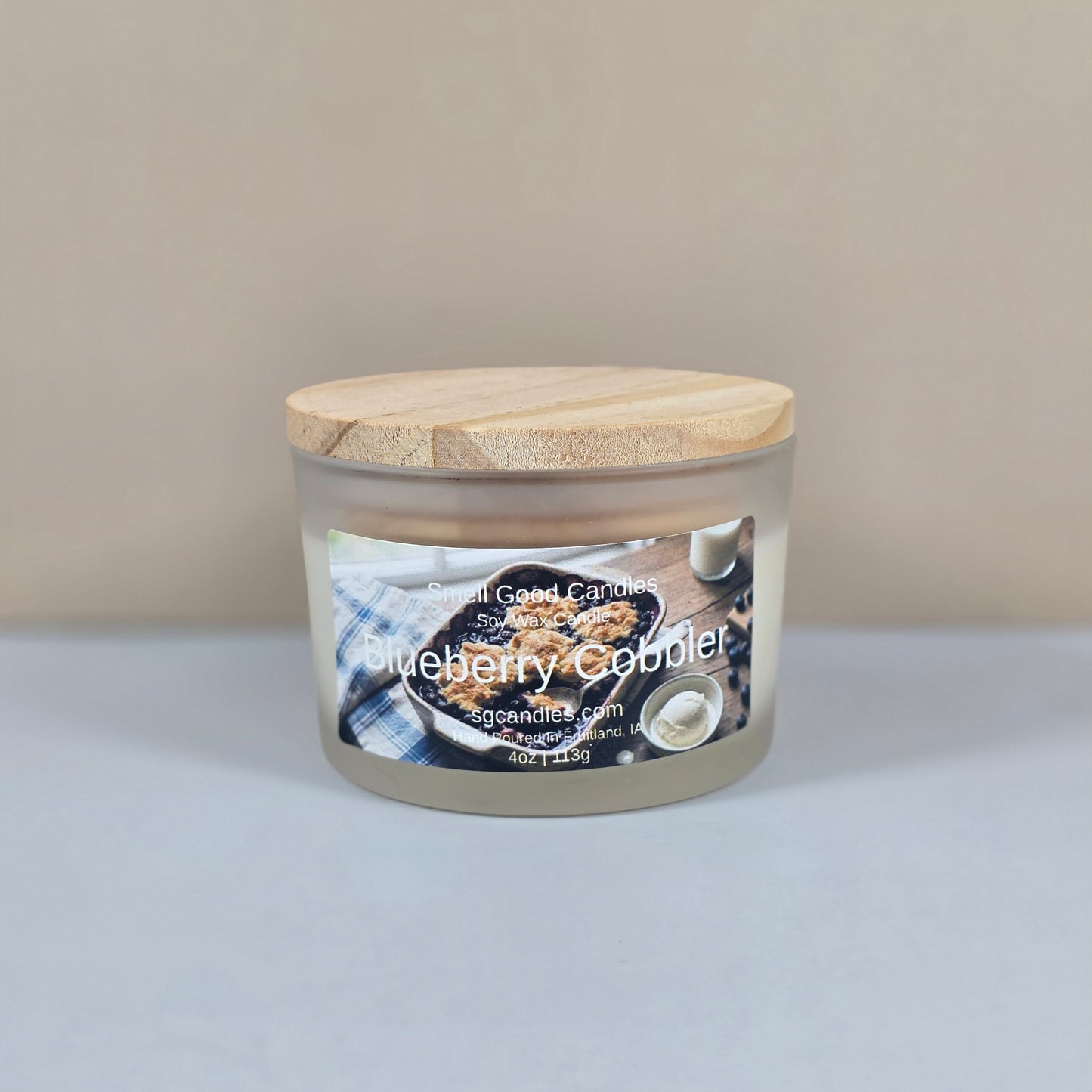 A 4oz clear glass jar candle with a black metal lid, featuring a "Blueberry Cobbler" label with a rustic illustration of a fresh blueberry dessert.