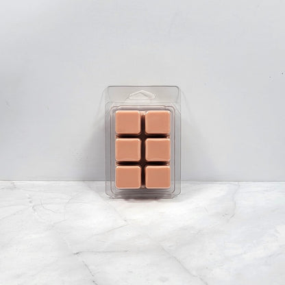 Pack of six tan-colored wax melts in clear packaging on a white marble surface with light gray background