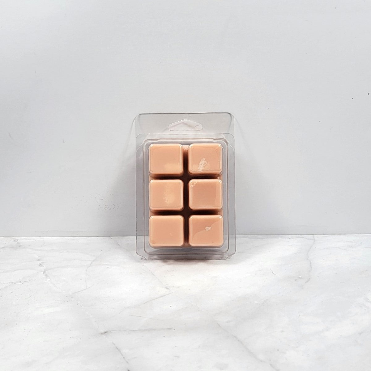 Pack of tan-colored wax melts in clear packaging on a white marble surface.