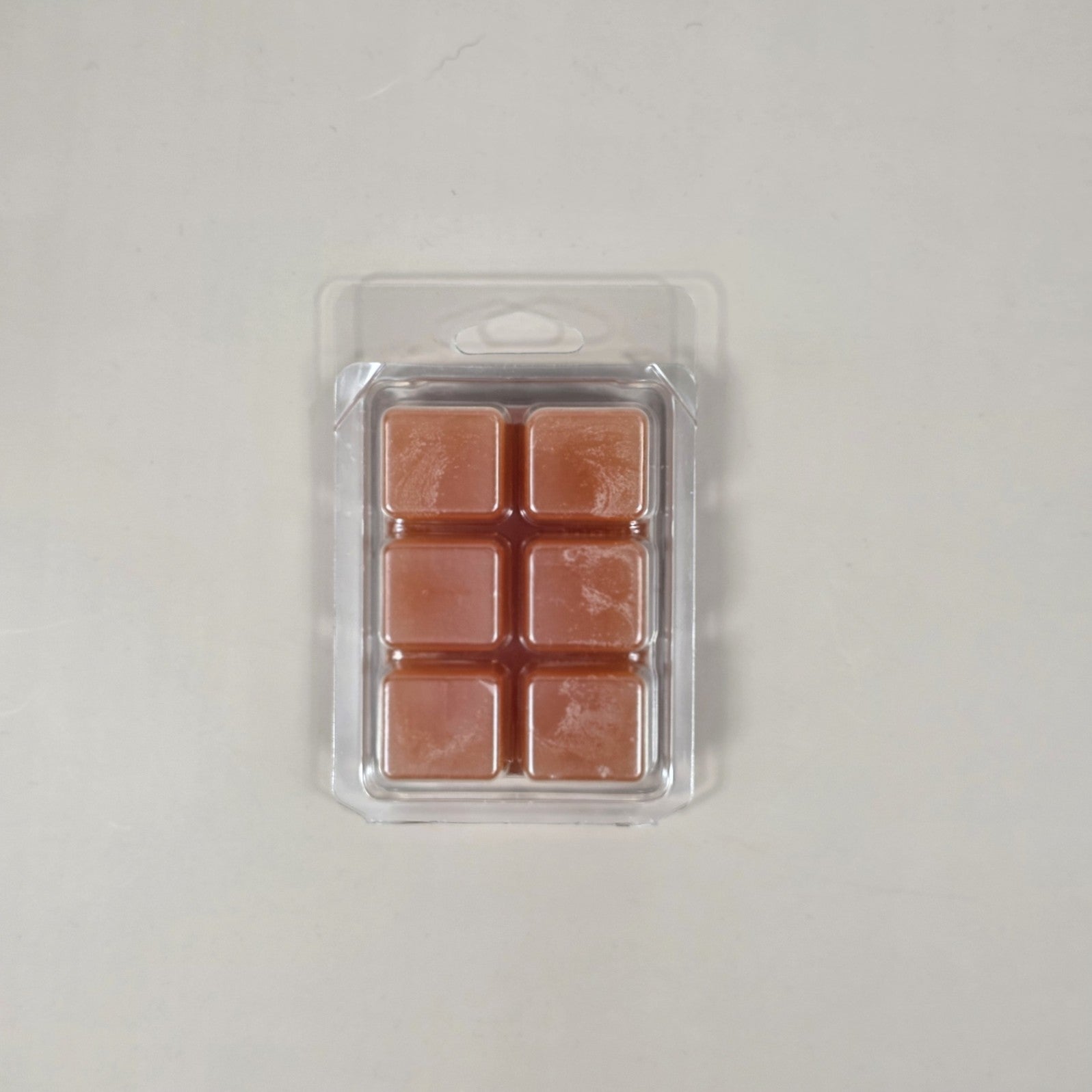 Pack of four square copper-colored wax melts in clear plastic packaging on a light gray background