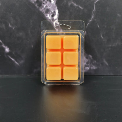 Pack of orange wax melts in clear packaging on a dark marble background