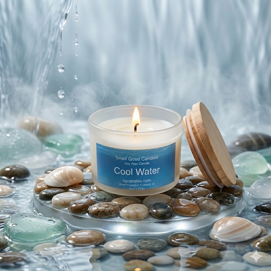Lit "Cool Water" frosted glass jar candle from Small Good Candles in a serene aquatic flat lay setting with smooth river stones, sea glass, shells, and flowing water.