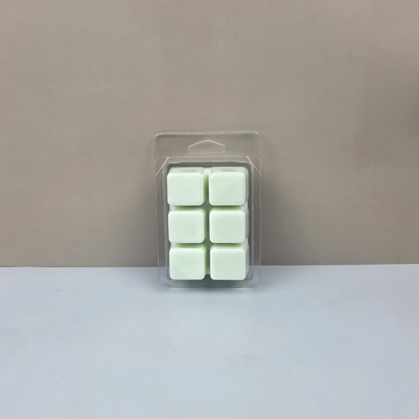 Pack of six green wax melts in clear packaging on a beige background