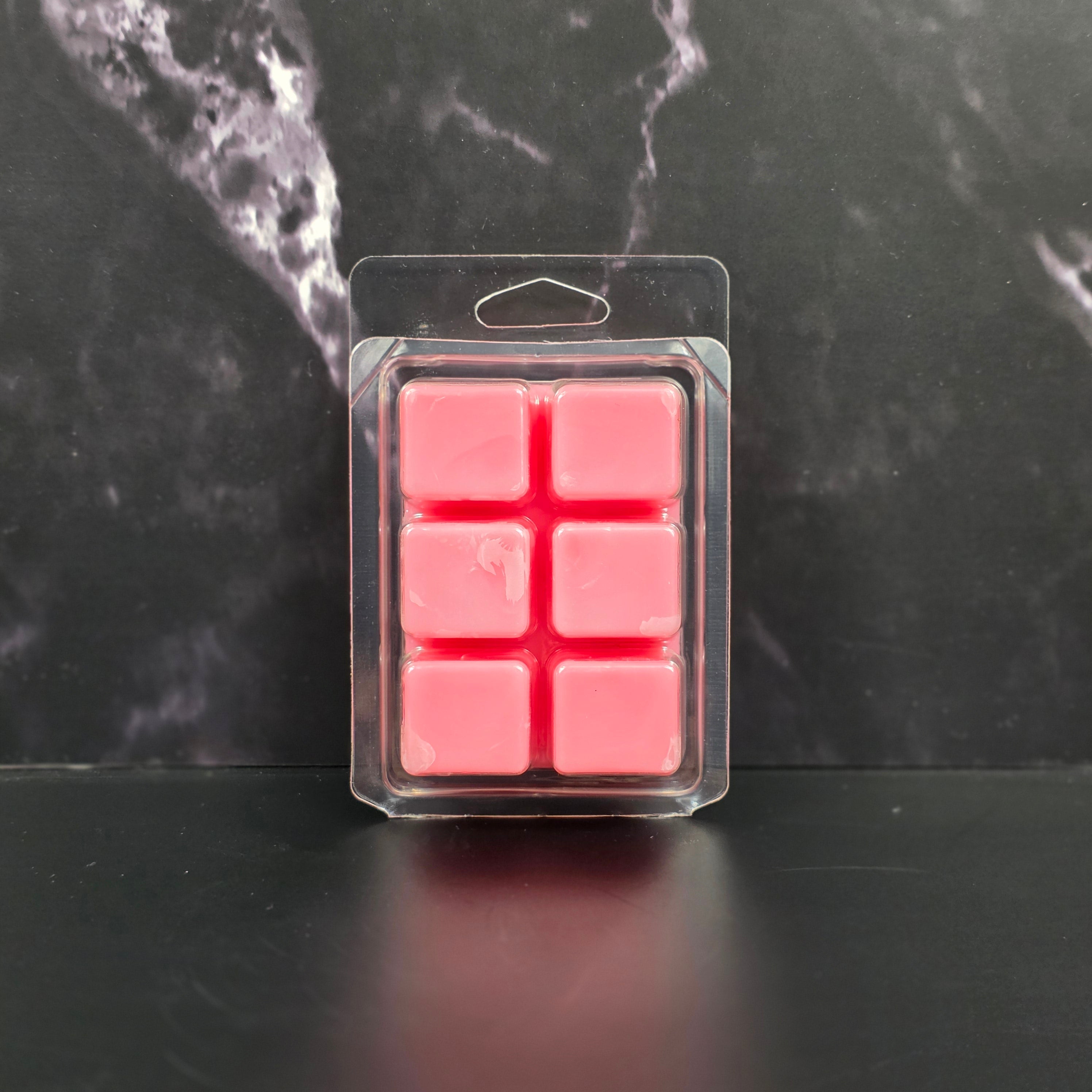 Pack of pink wax melts in clear packaging on a dark marble surface