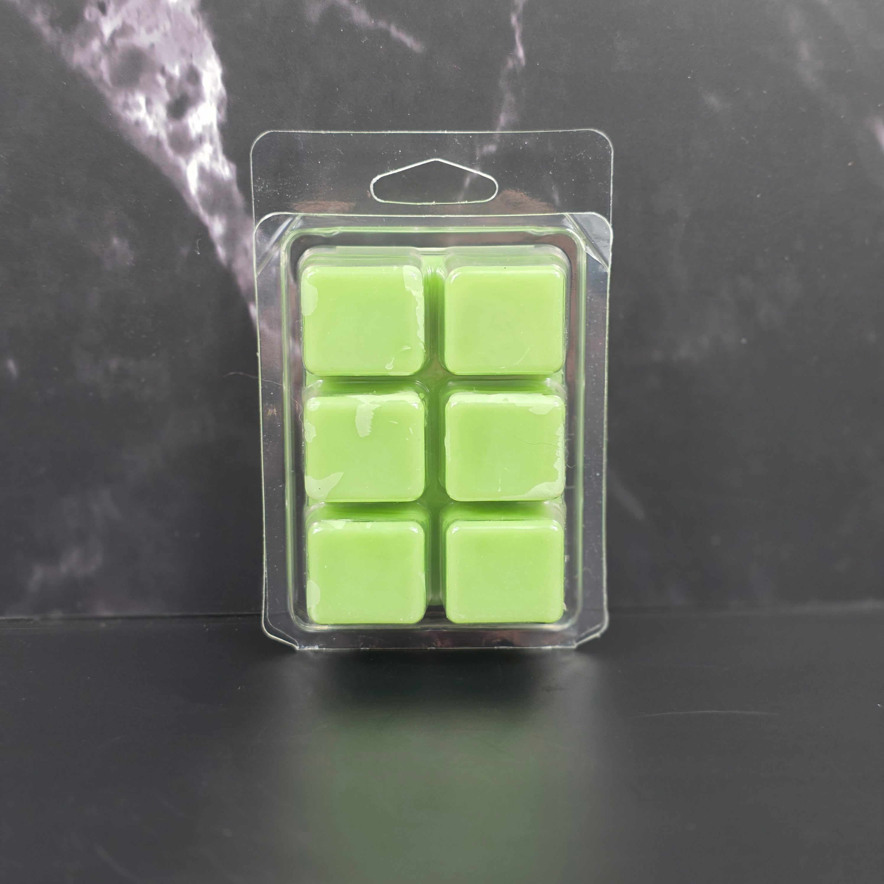 Pack of six green wax melts in clear packaging on a dark surface