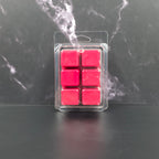 Pack of six red wax melts in clear packaging on a dark marble surface