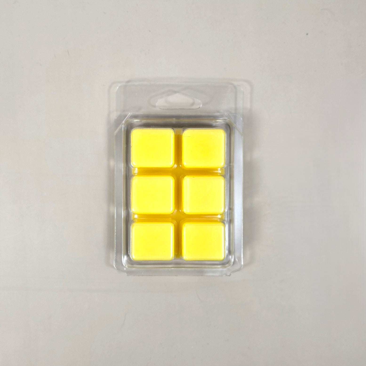 Underside view of a clear plastic 6-cube clamshell package showing bright yellow soy wax melt cubes.