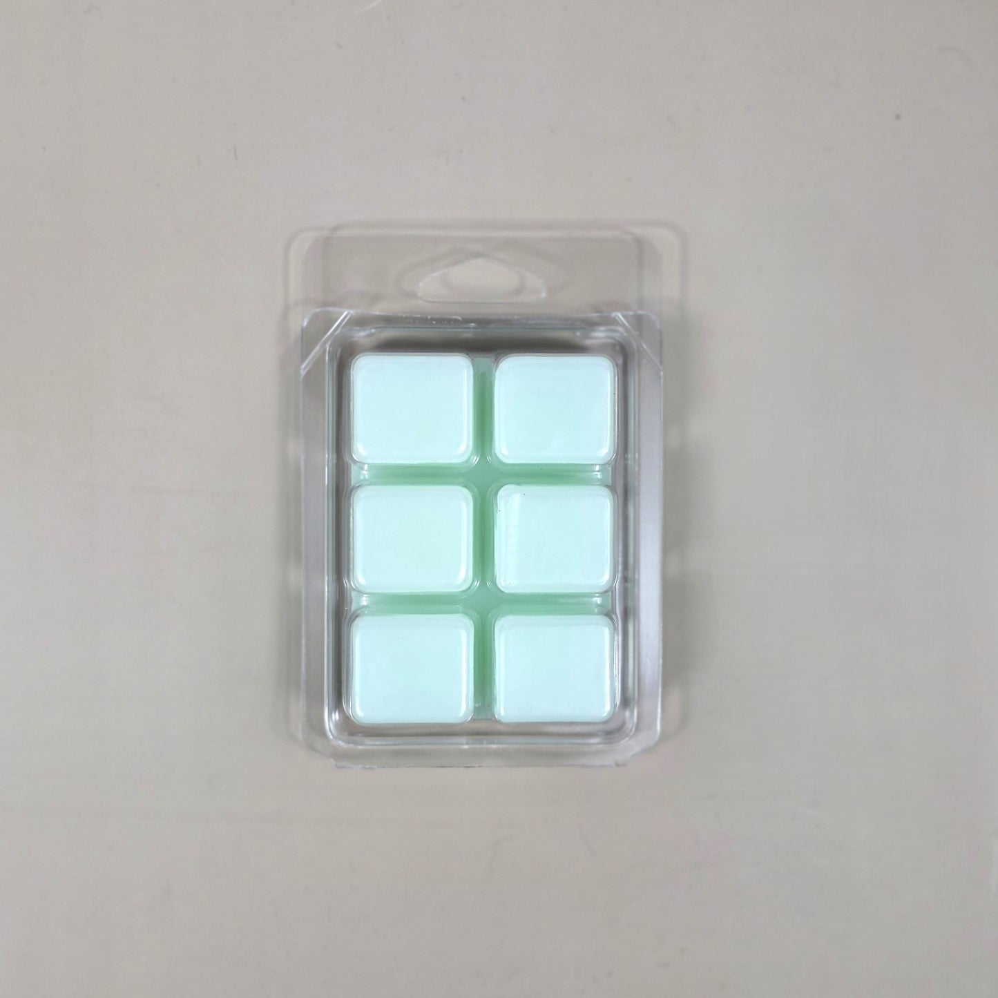 Underside view of a clear plastic 6-cube clamshell package showing light mint green soy wax melt cubes.