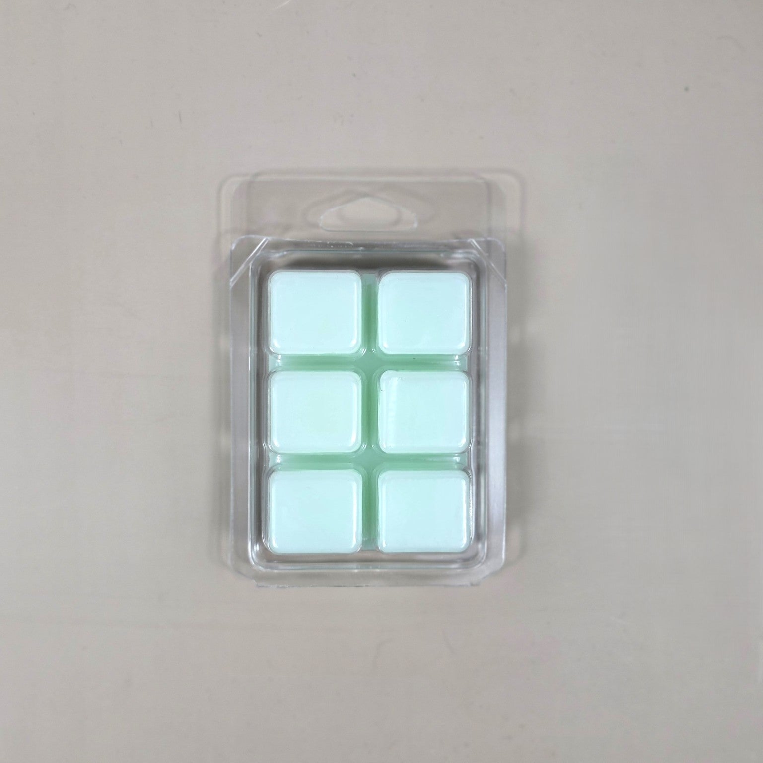 Underside view of a clear plastic 6-cube clamshell package showing light mint green soy wax melt cubes.