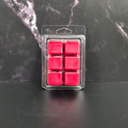 Pack of six red wax melts in clear packaging on a dark marble surface