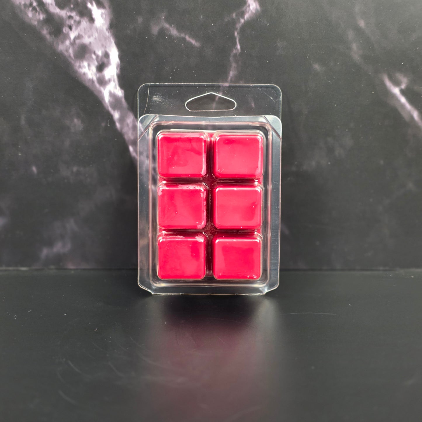 Pack of six red wax melts in clear packaging on a dark marble surface
