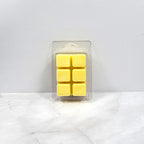 Pack of six yellow wax melts in clear packaging on a white marble surface.