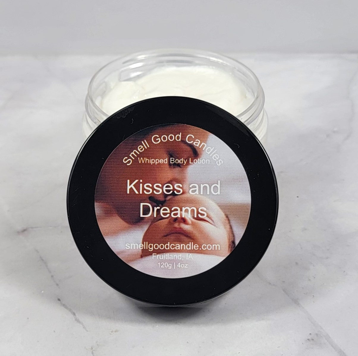Jar of 'Kisses and Dreams' whipped body lotion with a baby image on the label against a white marble background.
