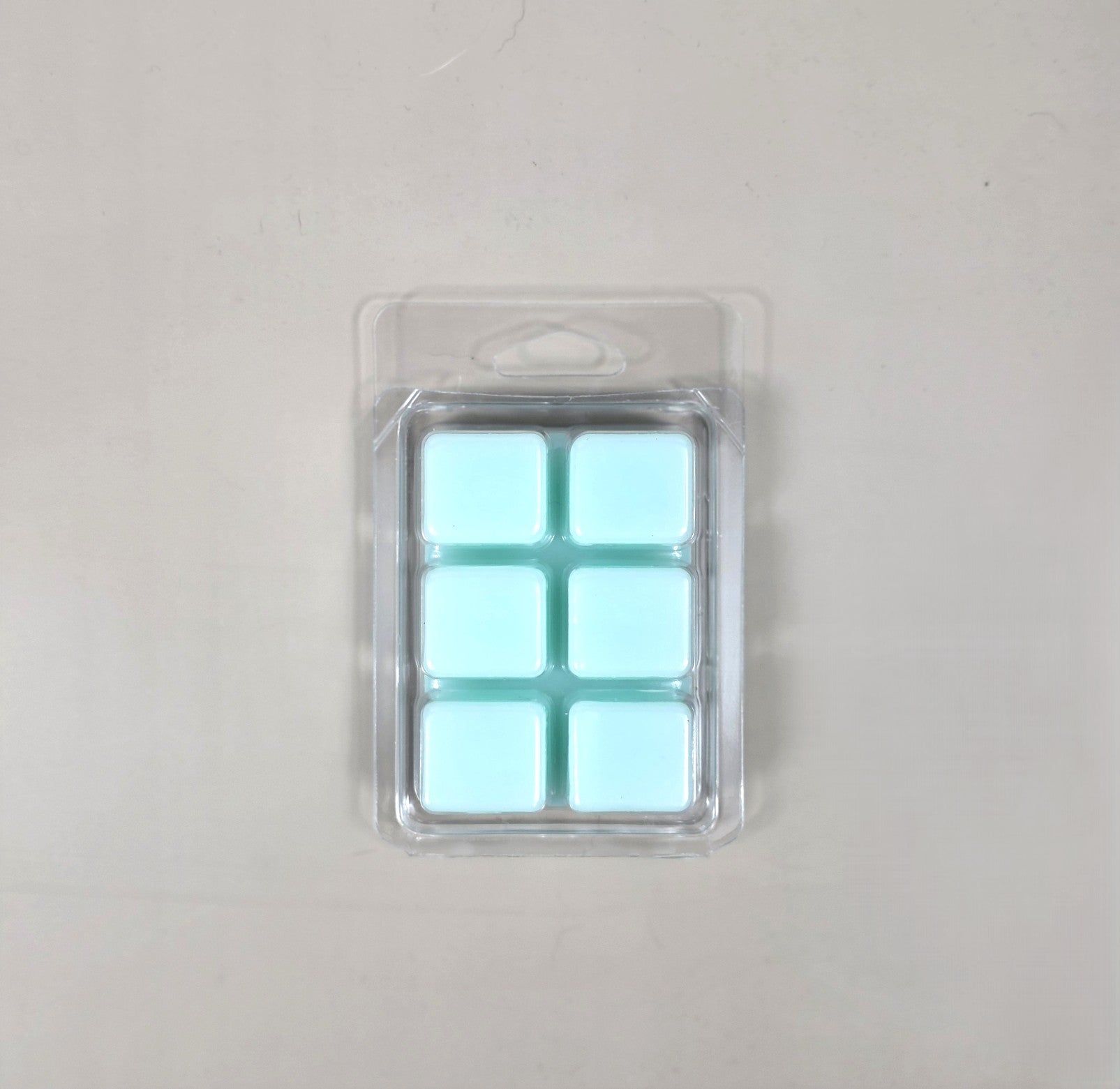 Underside view of a clear plastic 6-cube clamshell packaging showing light aqua blue soy wax melt cubes.