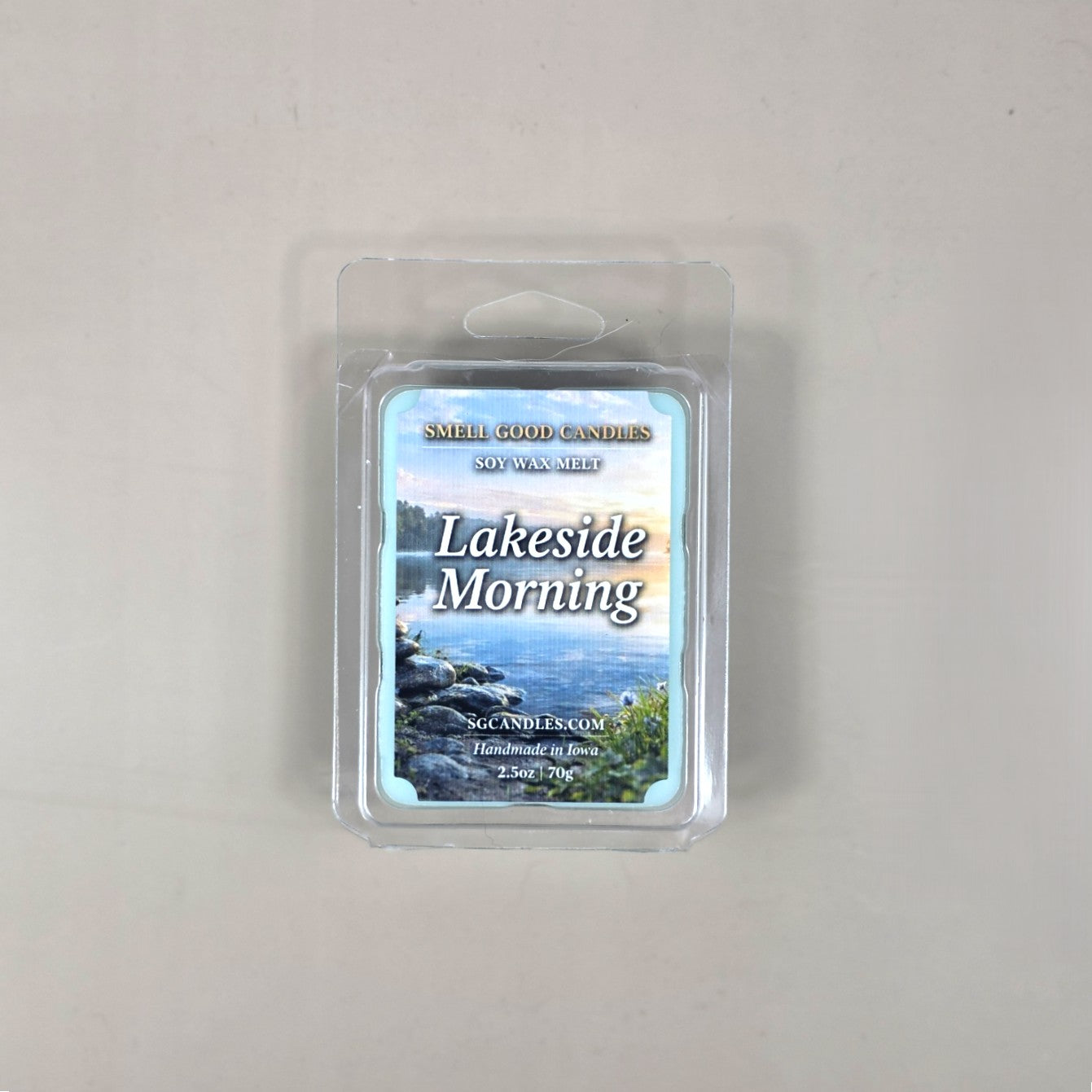 Top view of Lakeside Morning fragrance soy wax melt in a 2.5oz clear clamshell package featuring a scenic label of a calm lake shore at sunrise.