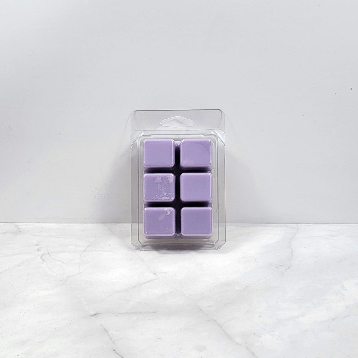 Pack of purple wax melts in clear packaging on a white marble surface