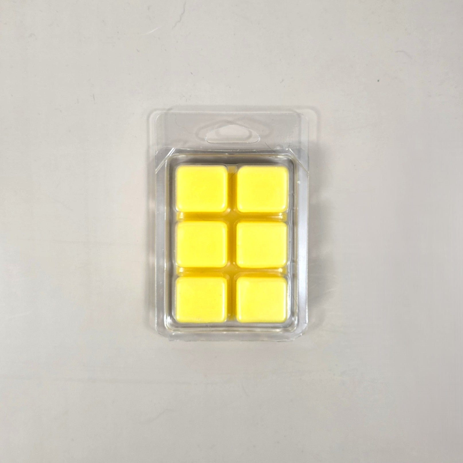 Underside view of a clear plastic 6-cube clamshell package filled with bright yellow soy wax melt cubes by Smell Good Candles.