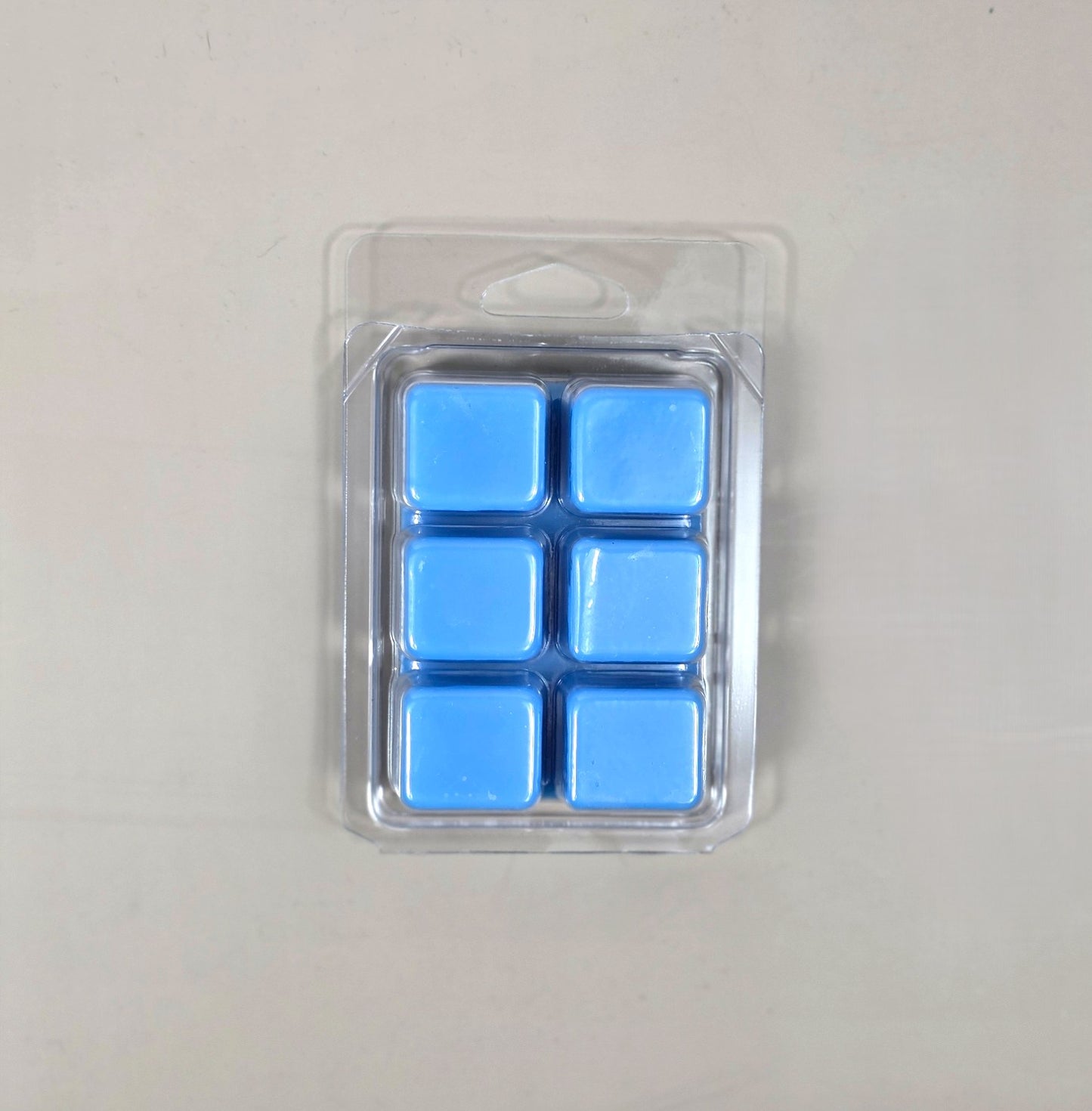 Underside view of a clear plastic 6-cube clamshell package showcasing vibrant periwinkle blue soy wax melt cubes.