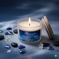 Lit "Moonlight Path" frosted glass candle by Smell Good Candles in a moody evening flat lay featuring white jasmine petals, polished black stones, and blue sea glass on a moonlit blue surface.