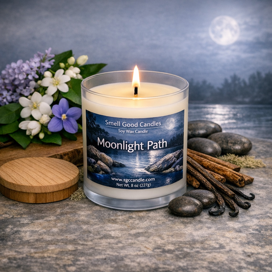 Moonlight Path soy wax candle in a white frosted glass jar with wooden lid, lit single wick, styled with soft florals, natural woods, and a calm moonlit setting.