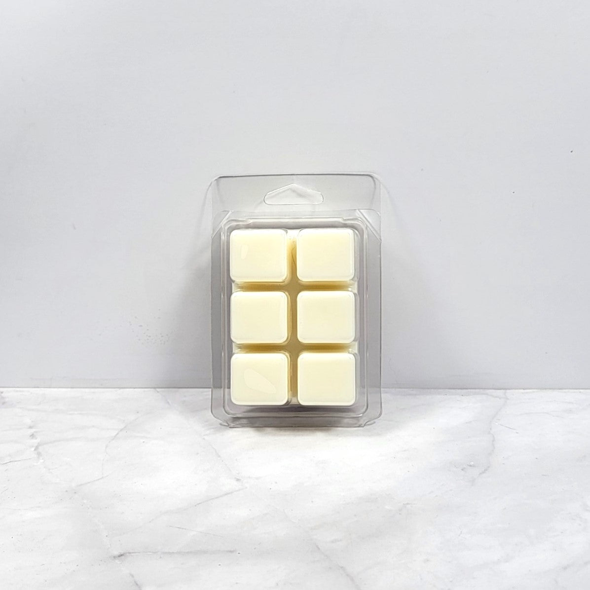 Pack of six cream-colored wax melts in a clear plastic packaging on a white marble surface.