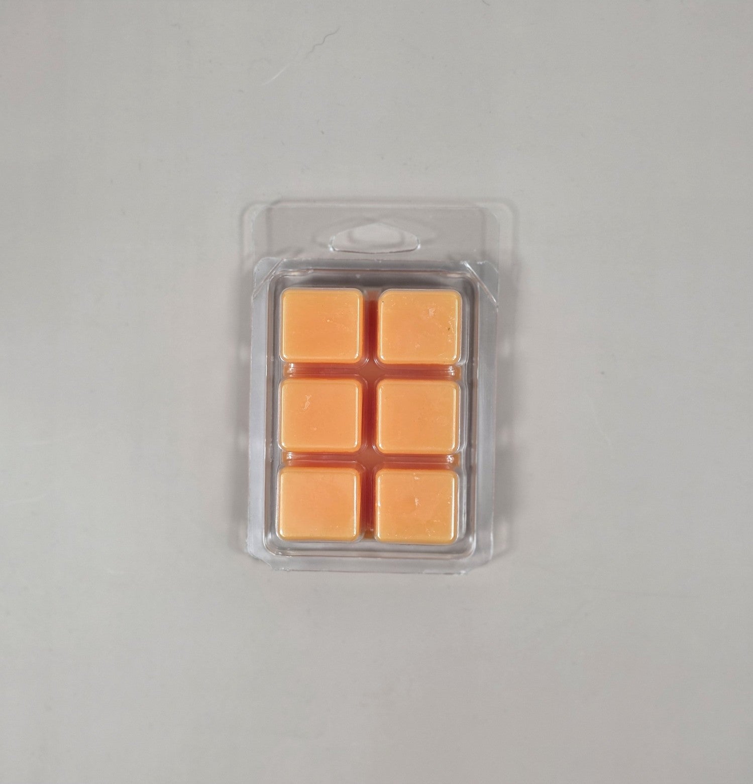 Pack of orange wax melts in clear packaging on a gray background