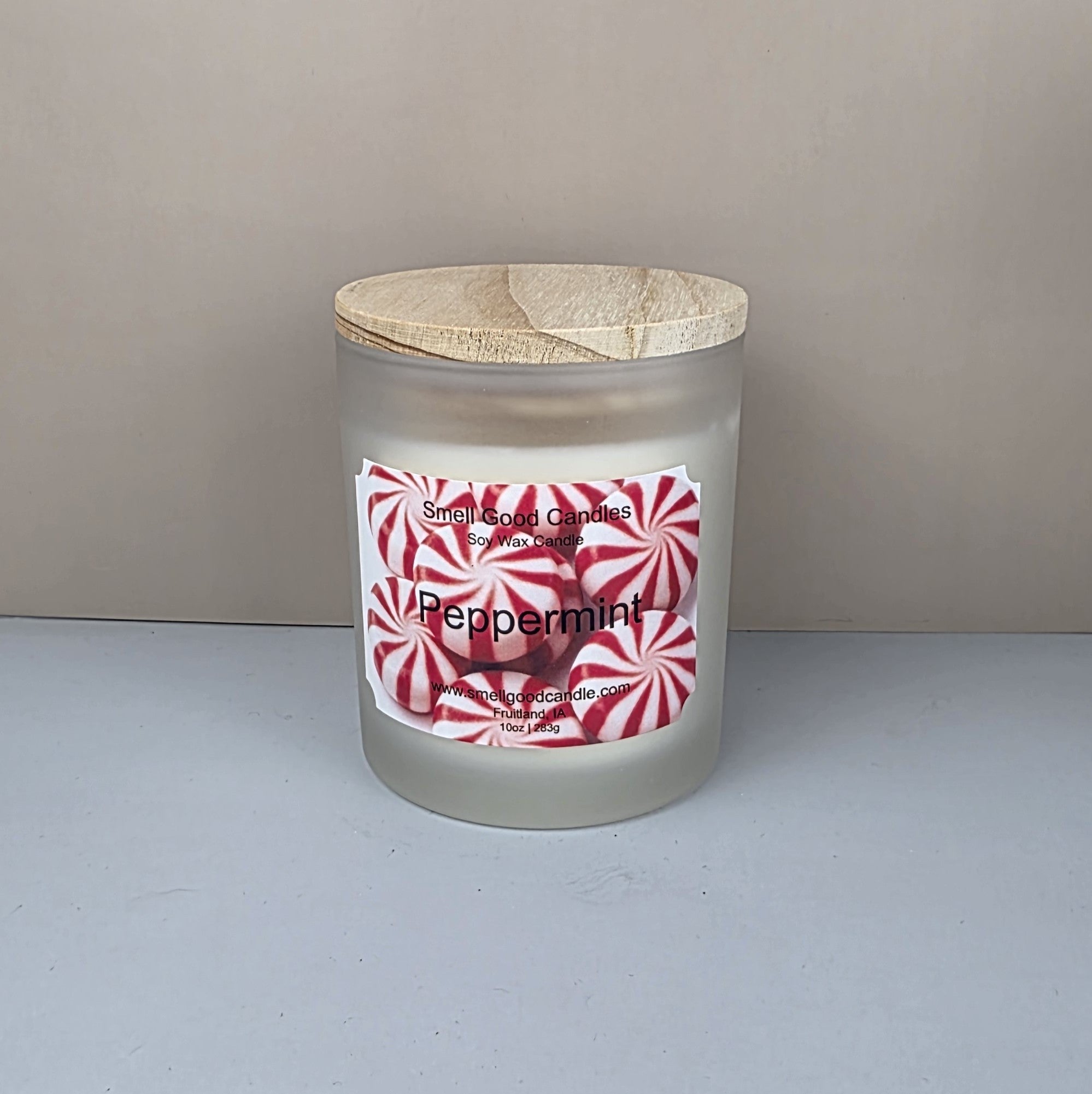 Frosted glass candle jar with wooden lid and peppermint-themed label on a neutral background
