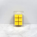 Pack of yellow wax melts in a clear plastic packaging on a white marble surface.