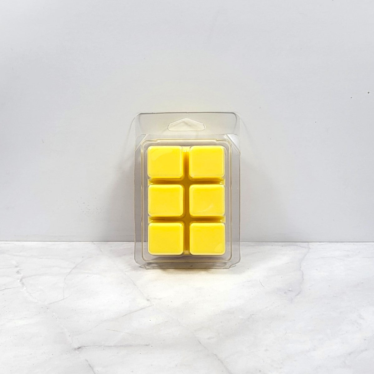 Pack of yellow wax melts in a clear plastic packaging on a white marble surface.