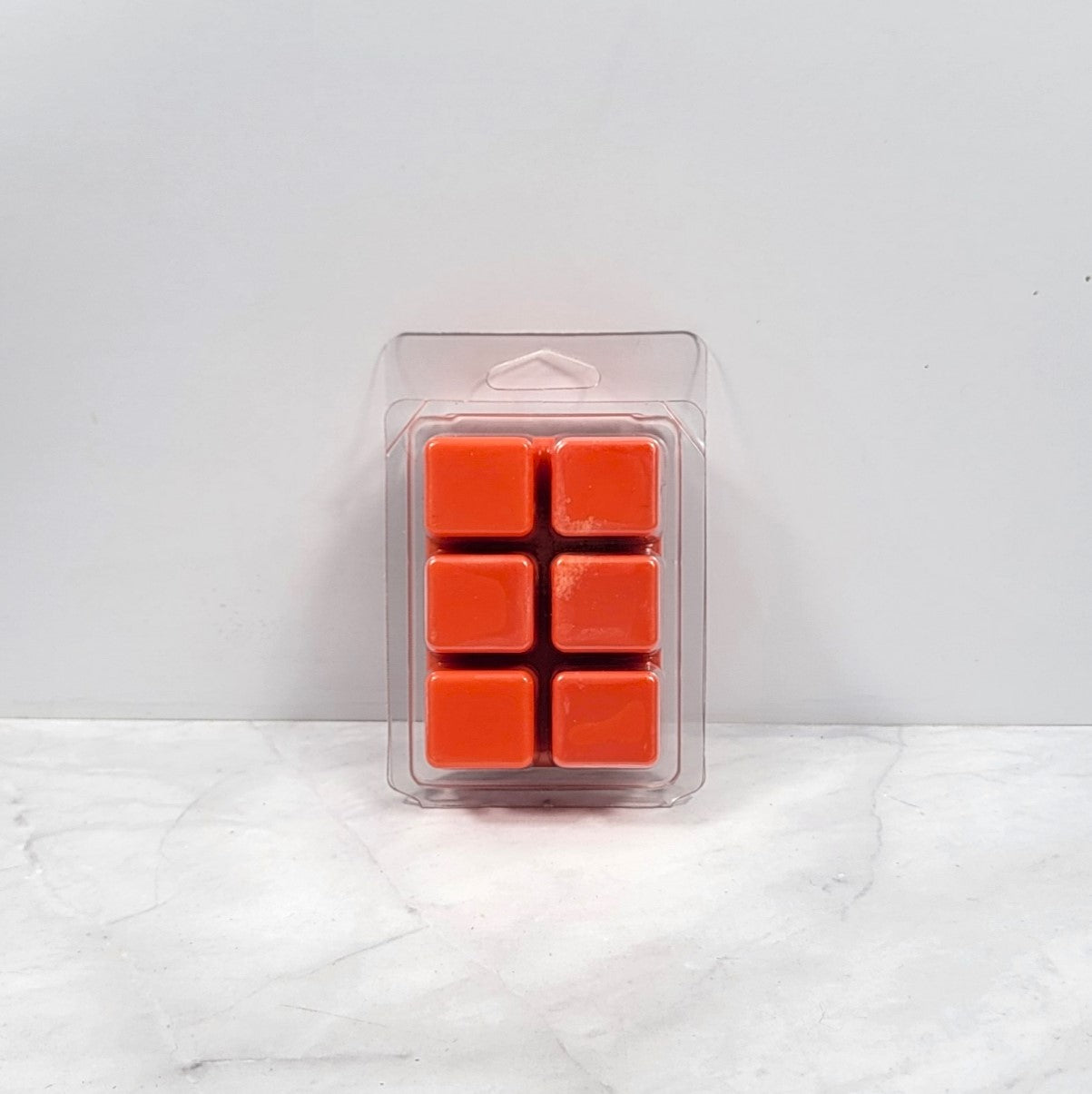 Pack of six orange wax melts in a clear plastic packaging on a white marble surface.