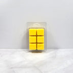 Pack of yellow wax melts in a clear plastic packaging on a white marble surface.