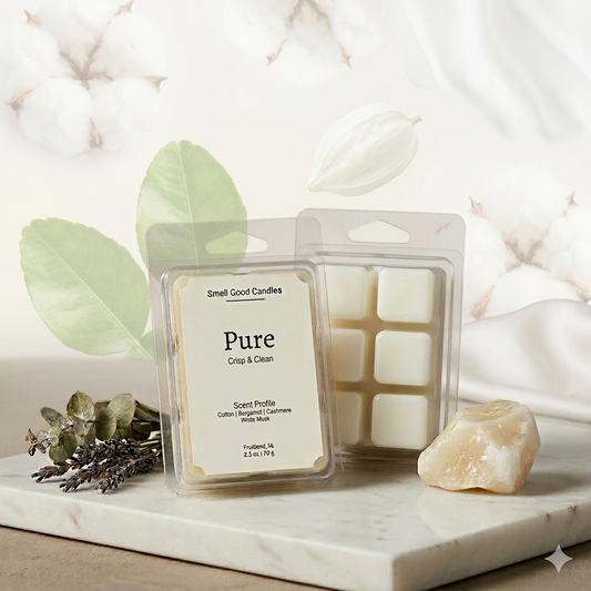 A luxury product photograph of "Pure" soy wax melts by Smell Good Candles, featuring a minimalist label with scent notes of cotton, bergamot, cashmere, and white musk. The clear clamshell packaging is displayed against an airy, bright background with soft cotton blossoms and fresh green citrus leaves, resting on a white marble slab with dried lavender and a natural quartz stone.