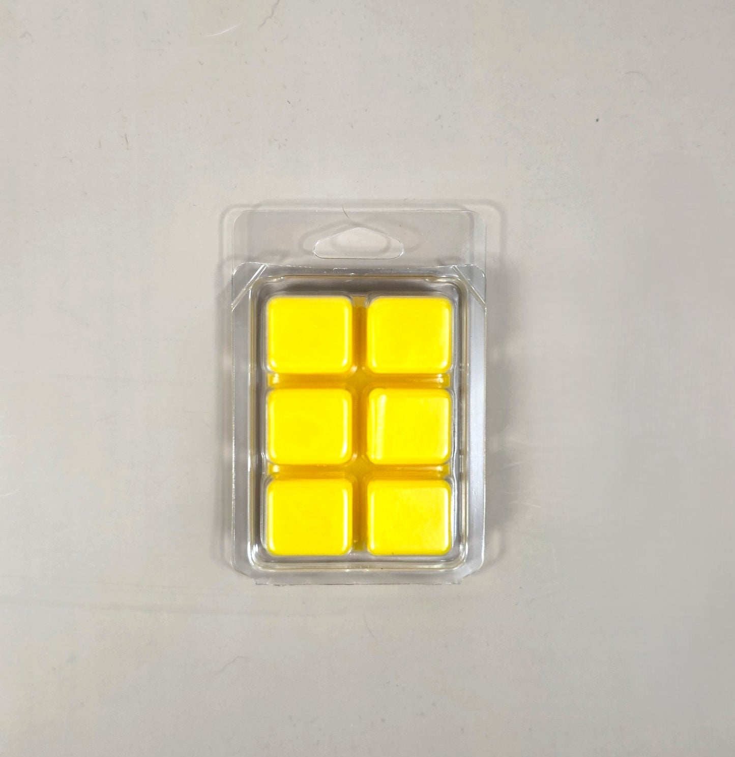 Underside view of a clear plastic 6-cube clamshell package filled with bright yellow soy wax melt cubes by Smell Good Candles.