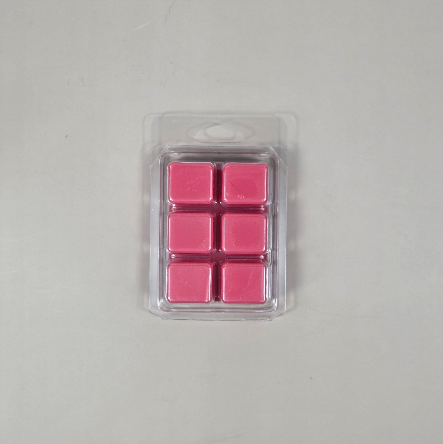 Pack of pink wax melts in a clear plastic packaging on a gray background
